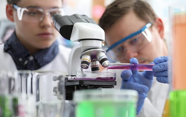 Man pours liquid into test tube under microscope