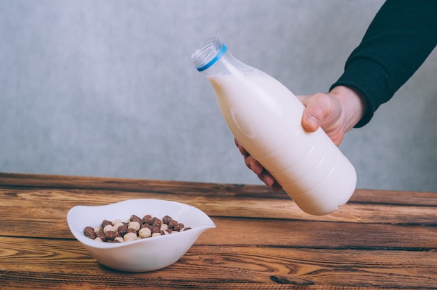 A man pours milk into cornflakes on a wooden.