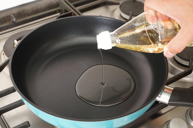 A man pours oil from a bottle into a frying pan in the kitchen Closeup Home cooking