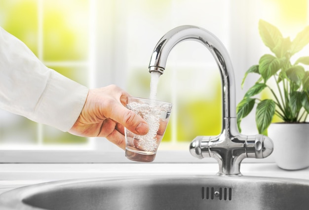 Man pours water from faucet into glass at home