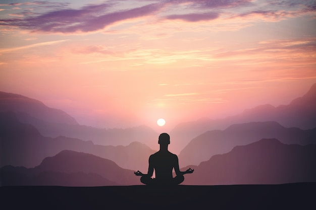 Man practices yoga and meditates on the mountain and sunset