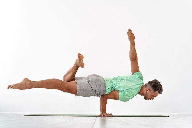 Man practicing balance yoga pose on white studio 