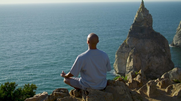 Man practicing yoga relaxation at ocean cliff edge Carefree guy meditating in