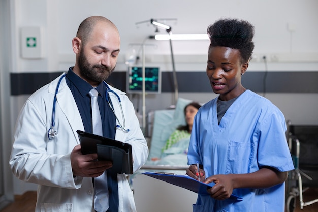 Man practitioner discussing with black assistant in hospital ward during medical consultation