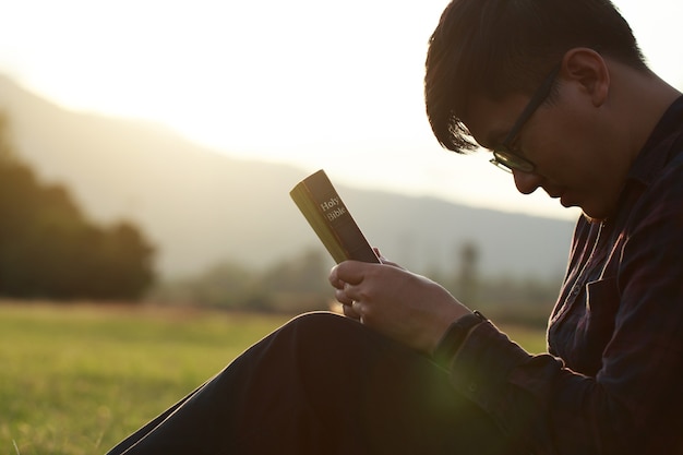 Man praying on the holy bible in a field during a beautiful sunsetmale sitting with closed eyes