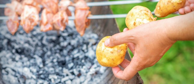 Man prepares barbecue meat with potatoes