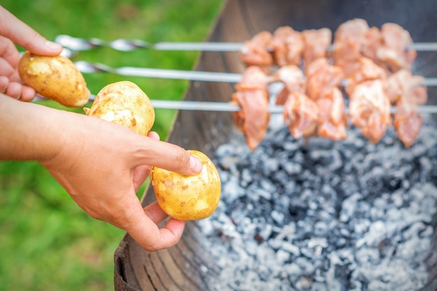 Man prepares barbecue meat with potatoes