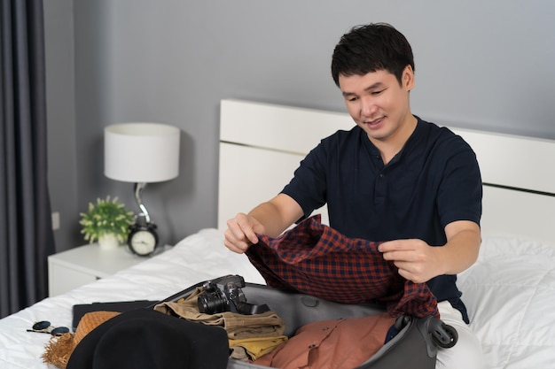 Man preparing and packing clothes into suitcase on bed at home holiday travel concept