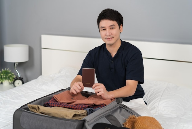 Man preparing passpord and packing suitcase on bed at home holiday travel concept