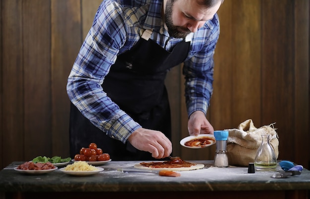 Photo a man preparing a pizza, knead the dough and puts ingredients