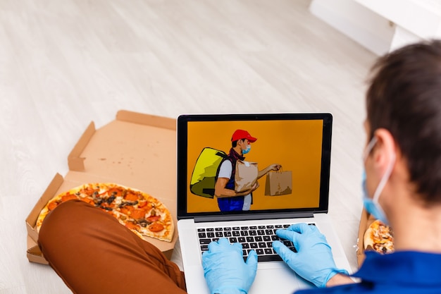 Photo man in protective gloves and mask using laptop for online food order during quarantine, closeup. delivery service