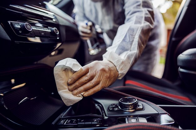 Man in protective suit with mask disinfecting inside car, wipe clean surfaces that are frequently touched, prevent infection of  coronavirus, contamination of germs or bacteria. Infection