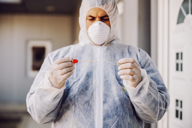 Man in protective suit with mask holding sample buccal cotton swab and test tube ready to collect DNA from the cells. Coronavirus covid-19. epidemic. World pandemic