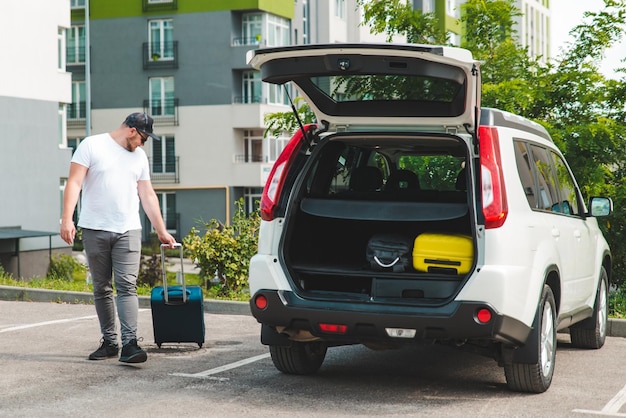 Man pull suitcase with wheels to car trunk