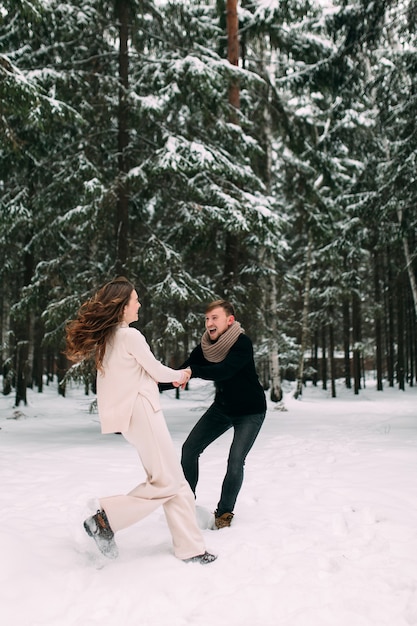 A man pulls a woman behind him in a snowy forest and smiles