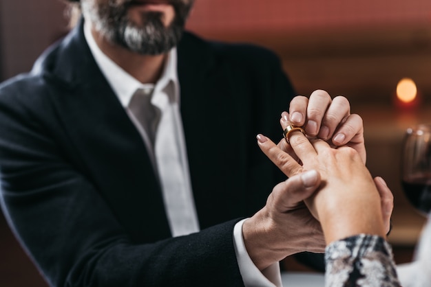 Man put ring on hand to his woman close-up. Focus on the ring