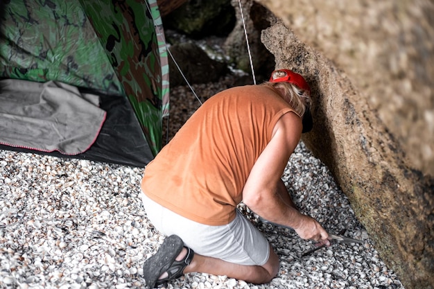 A man puts up a tourist tent in a stone grotto on a summer day Travel and tourism