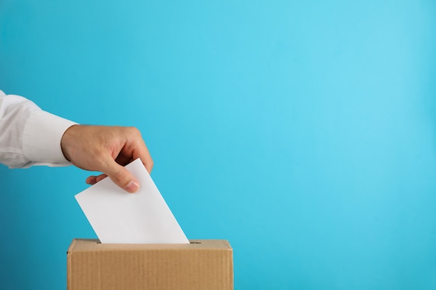 Man putting ballot into voting box on blue surface