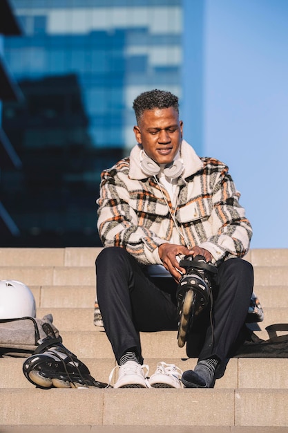 Man putting on his inline skates while sitting on a stair in a city park