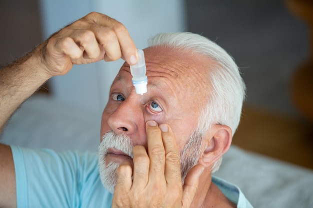 Man putting liquid drops in his eye solving vision problemSenior dropping eye drop medicine healing his eye pain Vision and ophthalmology medicine Senior gray hair man applying eye drop