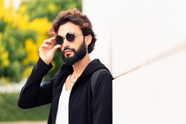 Man putting on sunglasses leaning in a white wall