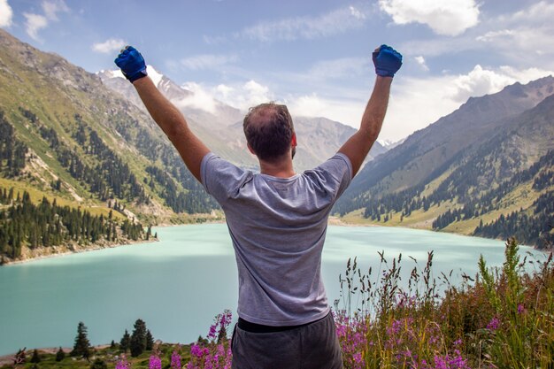 A man raised his hands to the sky against the backdrop of a mountain lake