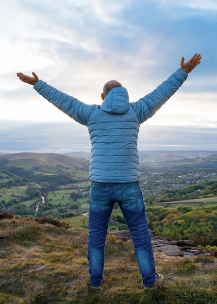 Man raising hands high and standing on top of mountain