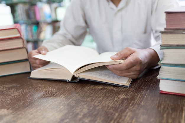 Man reading book with textbook stack on wooden desk