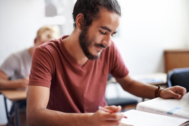 Man reading and classroom with book for thinking test or solution at university with education Person learning and assessment with writing pen and happy with studying for development at college