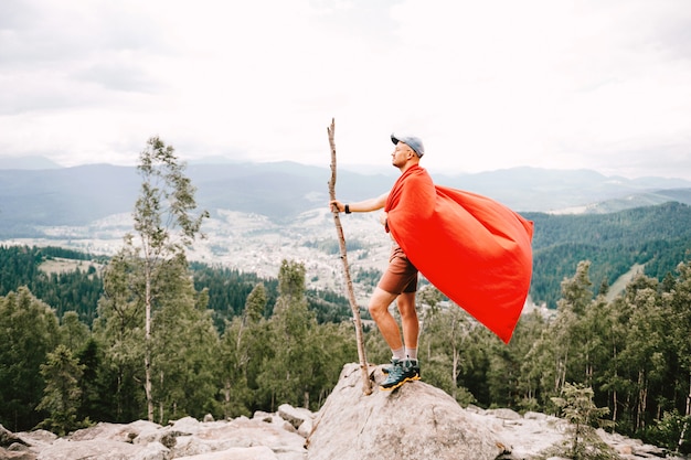 Photo man in red cloak standing on top of mountain with nature landscape