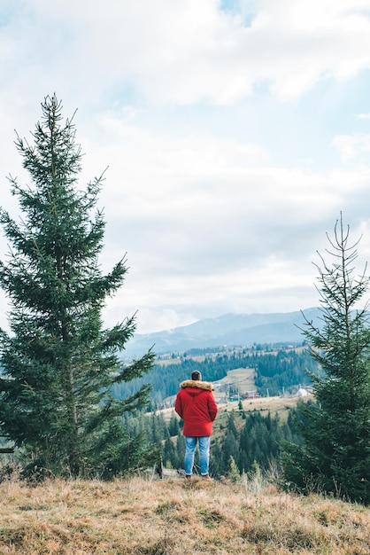 Man in red coat standing at the cliff with beautiful mountains view