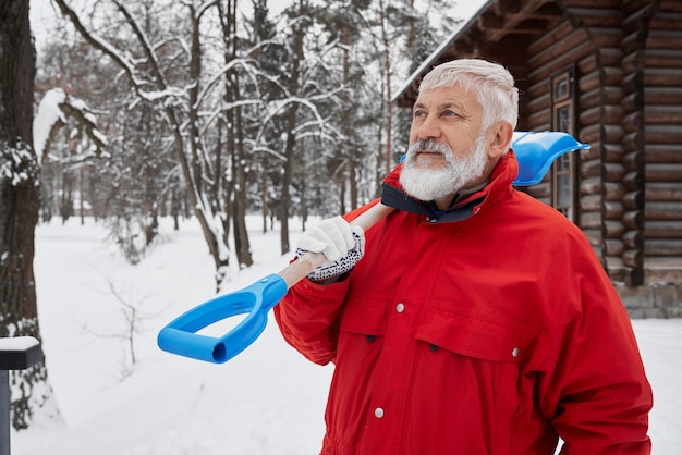 Man in red jacket with snow shovel on shoulder.