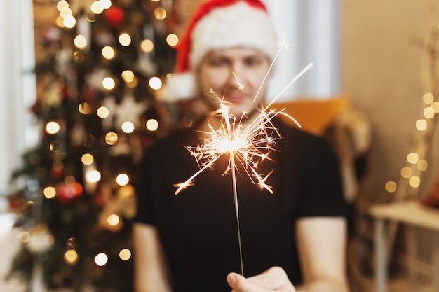 Man in red santa hat holding christmas or new year sparkler lights