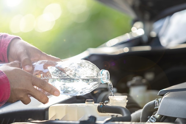 Man refill water to tank of car radiator and checking up the engine before start the trip Car maintenance or check up concept