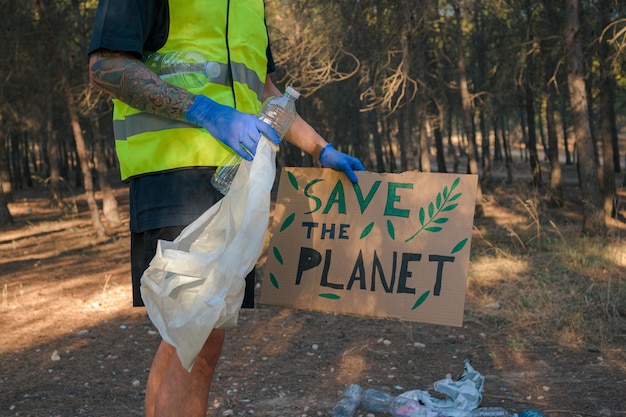 Man in reflective vest holding a sign and picking up plastic trash in a forest