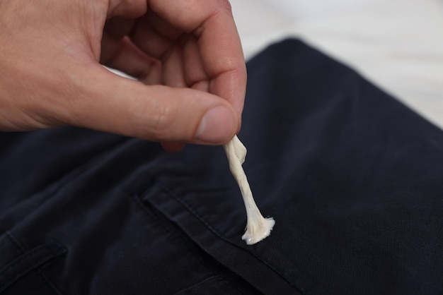 Man removing chewing gum from black jeans on white background closeup