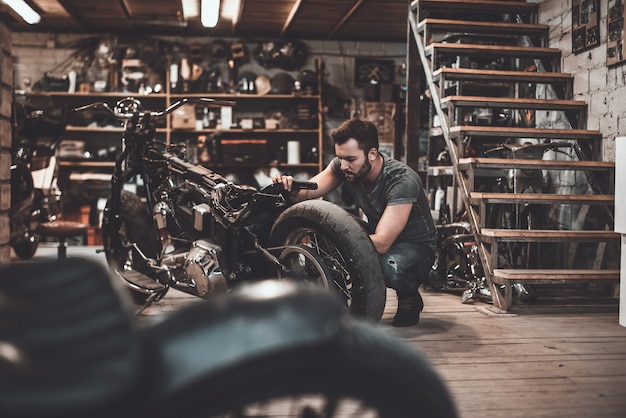 Man repairing bike. Confident young man repairing motorcycle in repair shop