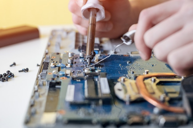 A man repairs a laptop, disassembles a laptop on a white wall, solders the laptop motherboard