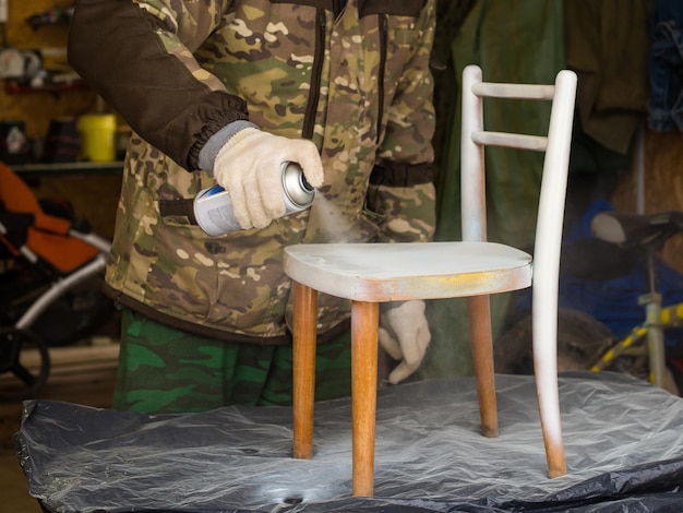 A man repairs old furniturepaints a children's chair with spray paint handmade concept