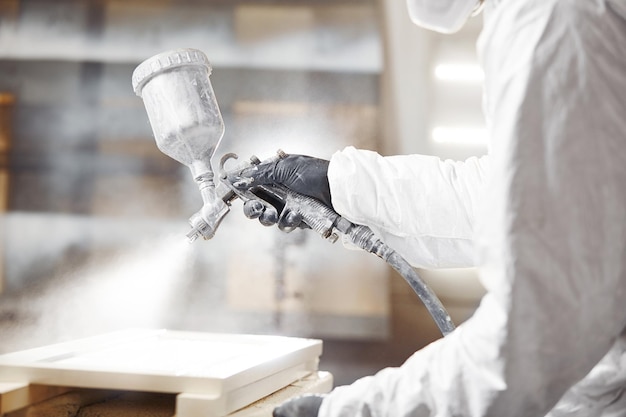 Man in respirator mask painting wooden planks at workshop Application of flame retardant ensuring fire protection airless spraying device