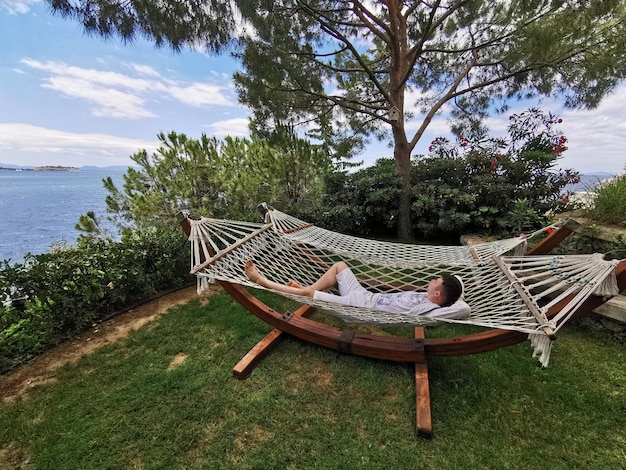 Man resting on a hammock under a pine tree near the sea