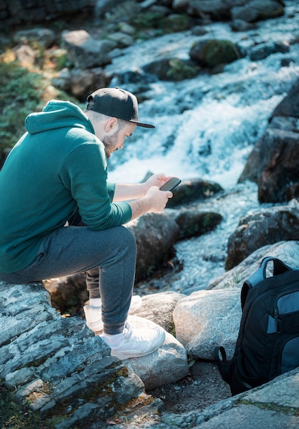 Man resting during hiking trip sitting on rock browsing his phone