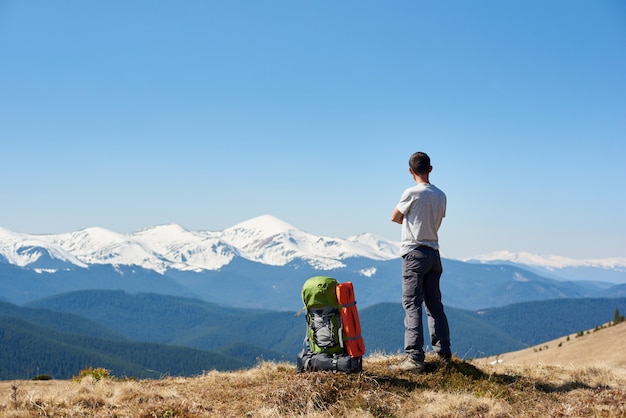 Man resting on top of the mountain after hiking enjoying stunning view of snowy mountains