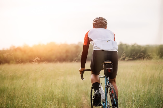 A man ride on bike on the road. Man riding vintage sports bike for evening exercise. A man ride bicycle to breathe in the fresh air in midst of nature, meadow, forest, with evening sun shining through