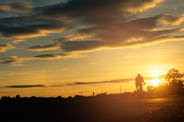 A man rides a bicycle on the road at sunset sky background.