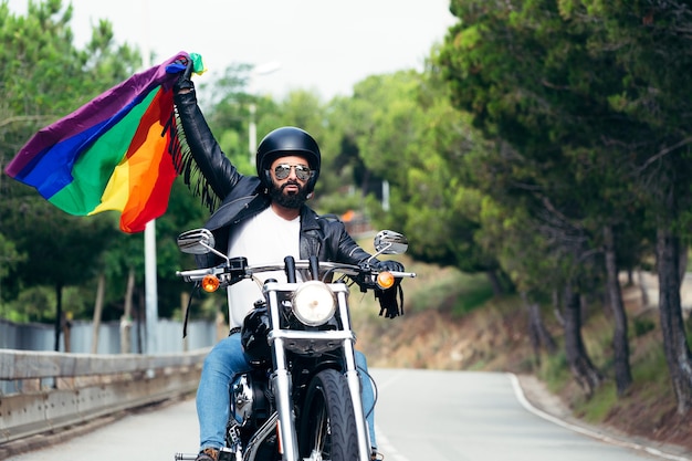 Man riding his motorcycle flying the rainbow flag