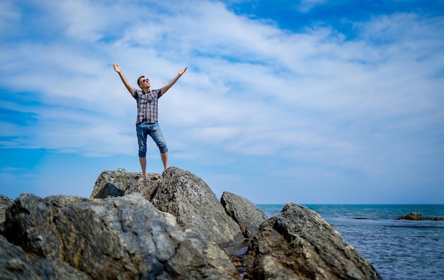 A man on a rocky shore raised his hands to the sky