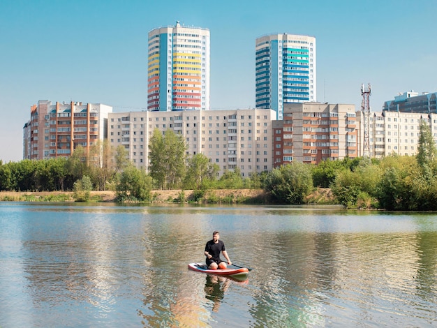 Man rowing on paddle surf board SUP in the lake in the city among the houses