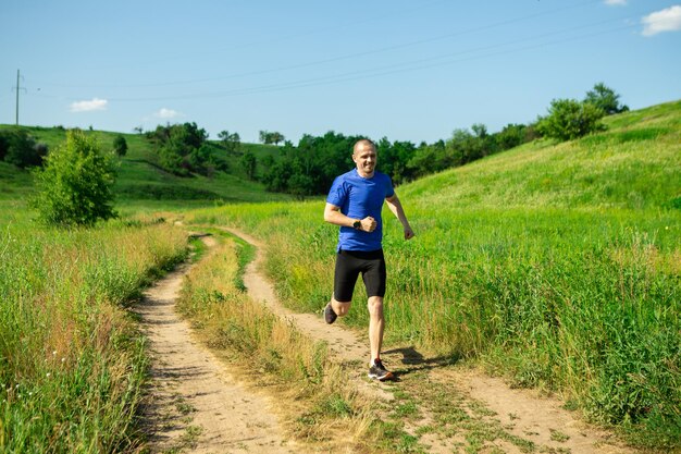 Man runner running on the rural road weared in sunglasses and blue t-shirt