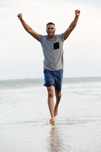 Man running barefoot on beach with arms raised in victory